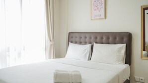 A neatly made bed with white linens and pillows, a white towel on the bed, and a framed map of London on the wall. - Elegant and Relaxing 1BR Asatti Apartment BSD (Pagedangan)