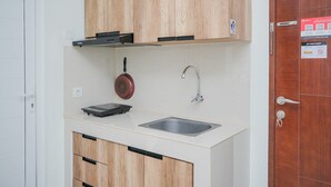 A compact kitchen with wooden cabinets, a stainless steel sink, and a red pan hanging on the wall. - Fully Furnished with Comfortable Design 2BR Apartment Springwood Residence (Tangerang)