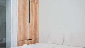 A modern bedroom with a wooden wardrobe, a neatly made bed, and a glass door leading to a bathroom. - Fully Furnished with Comfortable Design 2BR Apartment Springwood Residence (Tangerang)