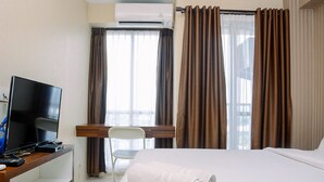 Una habitación de hotel con una cama, un televisor en un escritorio, aire acondicionado y cortinas.