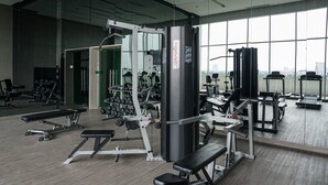 Ein Fitnessstudio mit unterschiedlichen Trainingsgeräten, großen Fenstern und einer Spiegelwand.