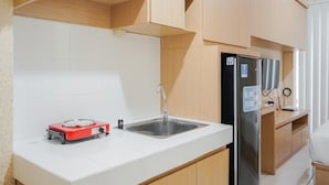 A compact kitchen with a sink, a red portable stove, a black refrigerator, and wooden cabinets. - Pool View Studio Apartment at M-Town Residence (Gading Serpong)