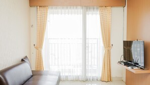 Een moderne hotelkamer met een bank, een televisie op een houten standaard en dunne gordijnen.