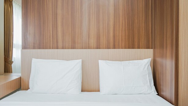 Een hotelkamer met een houten hoofdeinde, twee witte kussens en een netjes opgemaakt bed.
