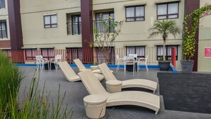Een terras op het dak met lounge fauteuils en tafels, omgeven door een lage hek en plantenbakken.