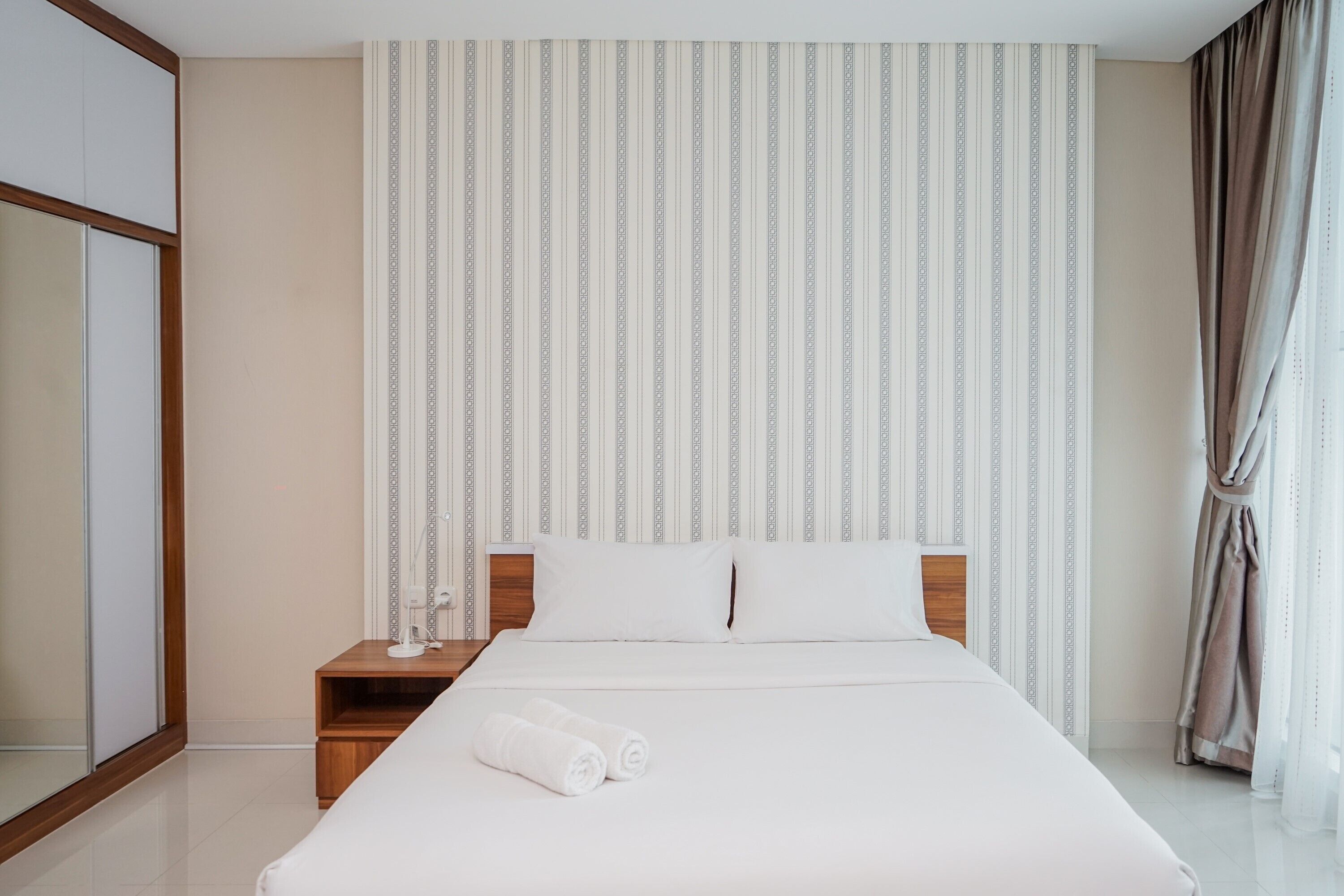 A hotel room with a large bed, a nightstand, a mirror, and a window with curtains.