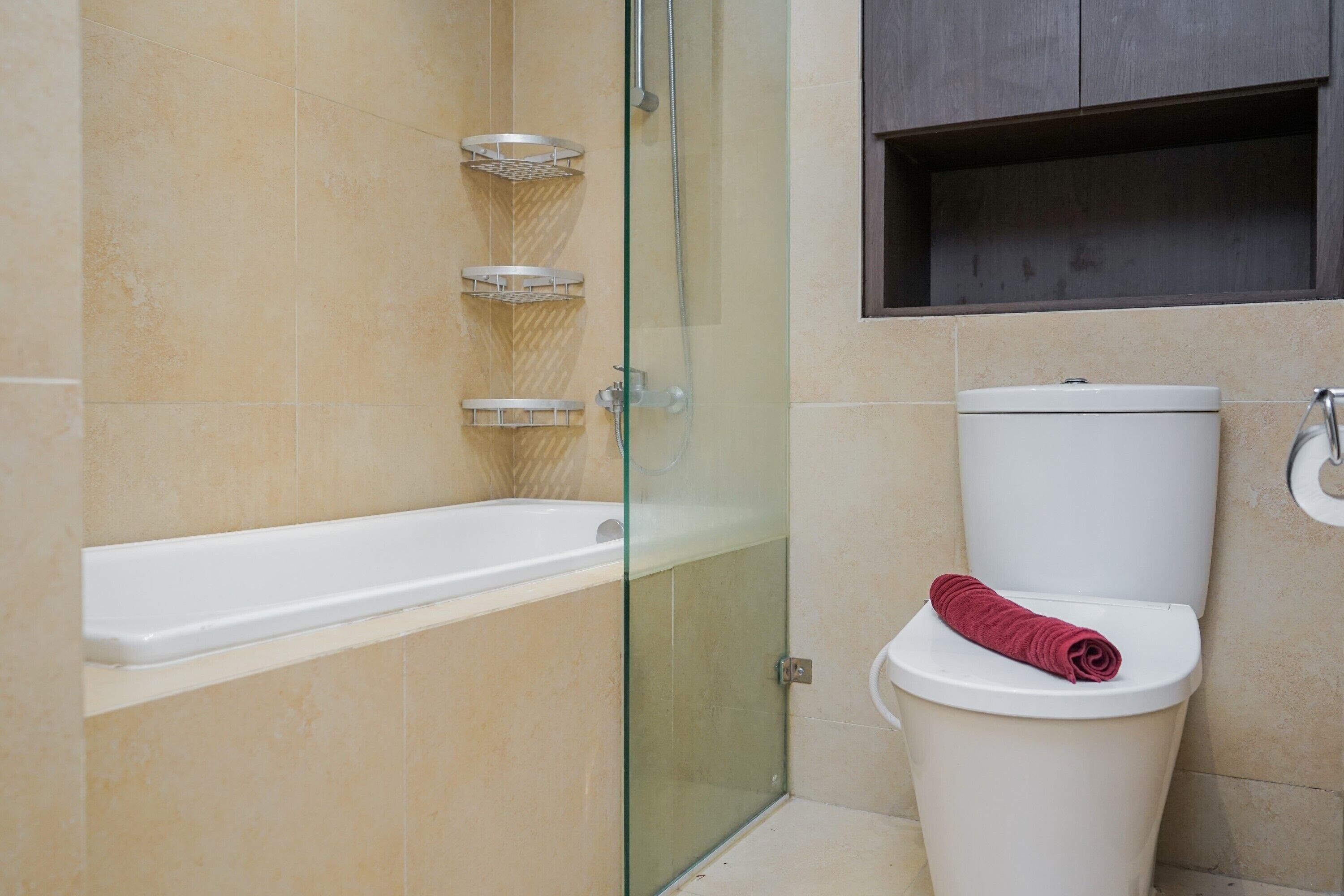 Une salle de bain avec une douche à parois de verre, une baignoire blanche et des toilettes sur lesquelles est posée une serviette rouge.