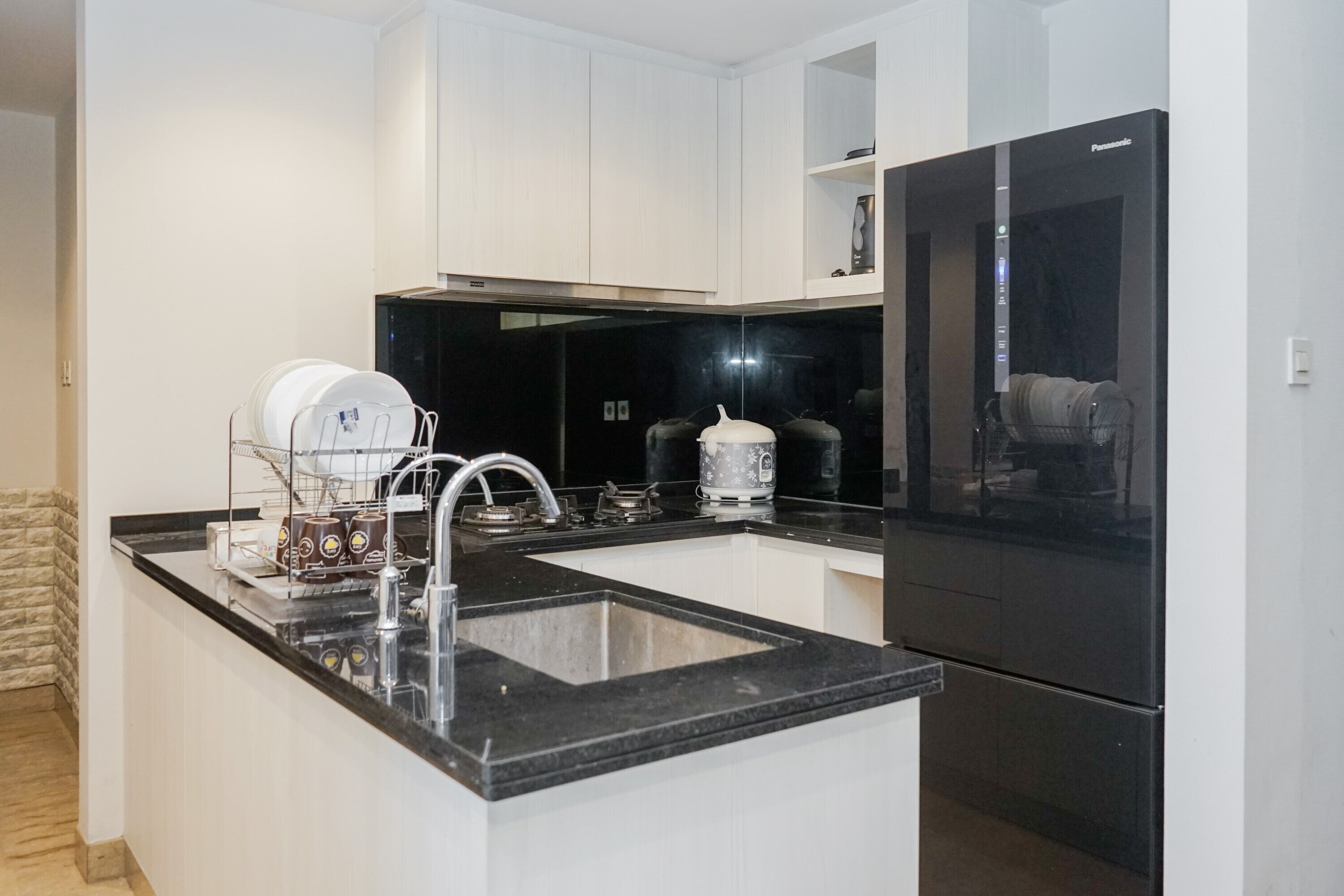 A modern kitchen with white cabinets, a black countertop, a sink, a stove, and a black refrigerator.