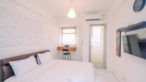 A hotel room with a bed, a desk, a chair, a TV, and a clock on the wall.