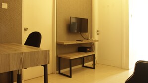 A room with a wooden table, a black chair, a television mounted on the wall, and a door.