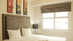 A hotel room with a large bed, a headboard, a window with curtains, and wall art depicting landmarks.