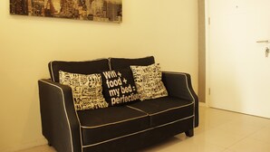 A black sofa with patterned cushions against a white wall, a cityscape painting above, and a closed door to the right.