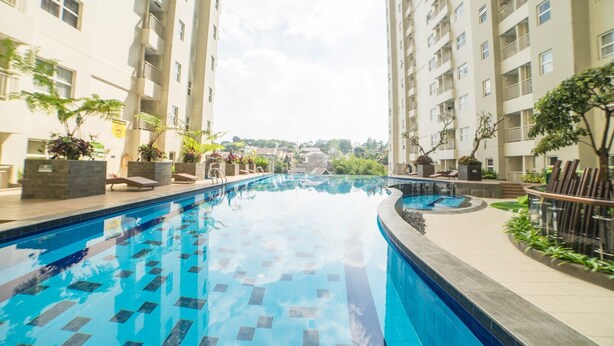 A swimming pool surrounded by high-rise buildings with balconies, potted plants, and a clear sky.