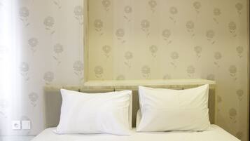 A hotel room with a bed, two white pillows, a wooden headboard, and floral wallpaper.