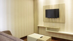 A modern hotel room with a flat-screen TV mounted on the wall, a small bedside table, and a sofa. - Homey and Chic 2BR Apartment Newton Residence (Bandung)