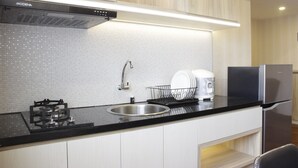 A modern kitchen with a black countertop, stainless steel appliances, and a tiled backsplash. - Homey and Chic 2BR Apartment Newton Residence (Bandung)