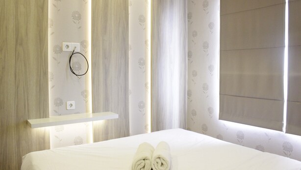 A neatly made bed with rolled towels, a bedside table with a power outlet, and a window with curtains. - Homey and Chic 2BR Apartment Newton Residence (Bandung)
