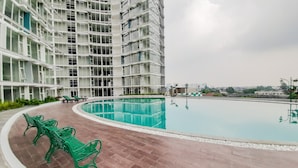 Un edificio moderno con piscina, bancos de metal verde y un camino pavimentado.