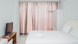 Habitación de hotel con una cama, un televisor sobre un soporte de madera, un armario y una cortina.