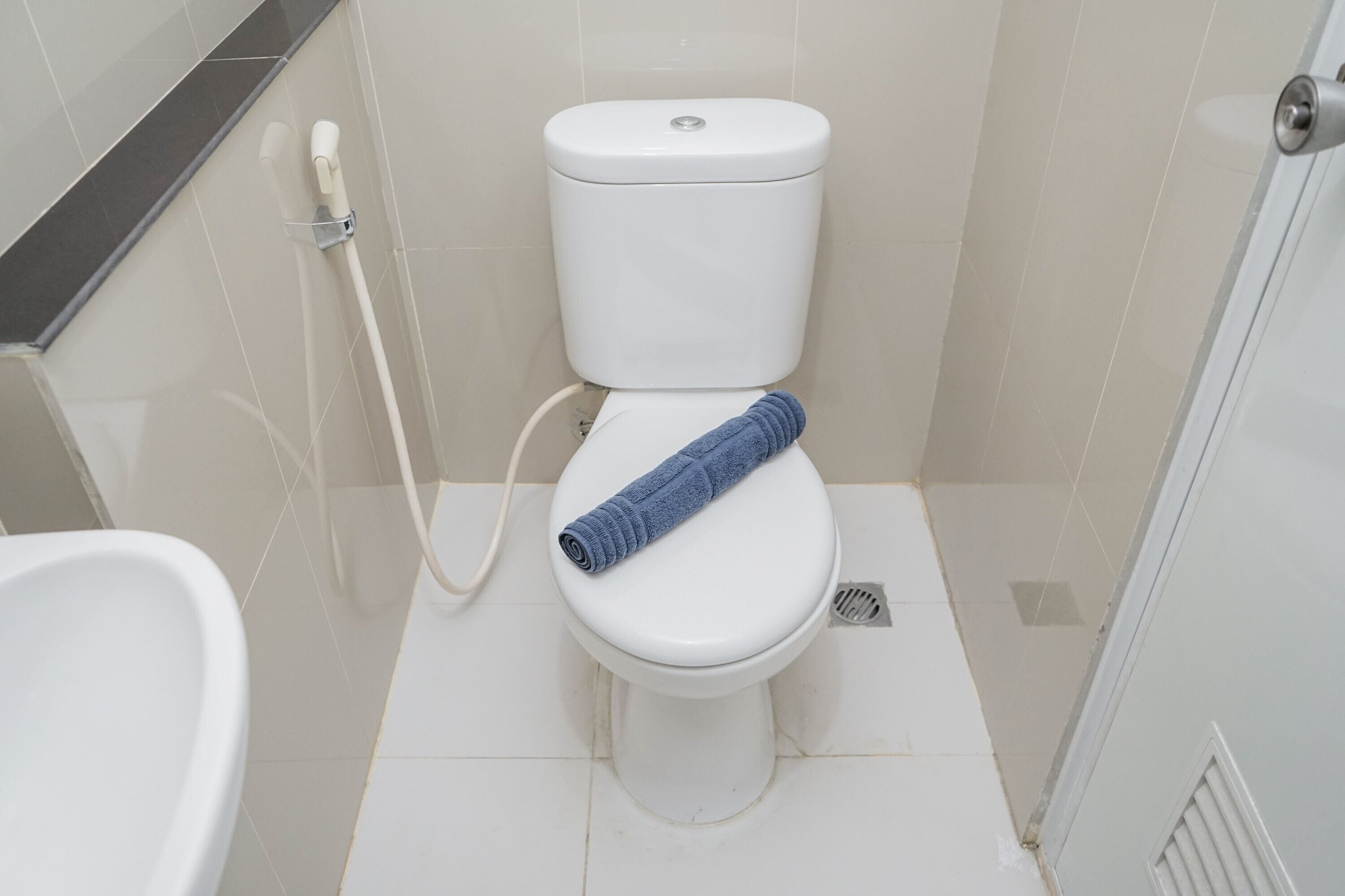A white toilet with a blue towel on the seat, a white bidet, and a shower area with a glass door.