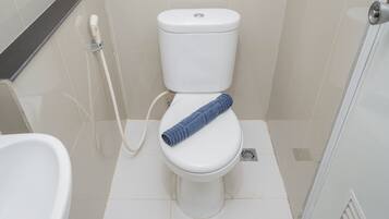 A white toilet with a blue towel on the seat, a white bidet, and a shower area with a glass door.