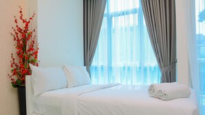 A neatly made bed with white linens, a potted red plant, and sheer curtains. - Best Location and New Furnished @ Studio Capitol Park Residence Apartment (Jakarta)
