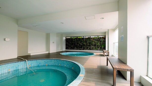 A modern indoor swimming pool area with two pools, wooden flooring, and a bench. - Best Location and New Furnished @ Studio Capitol Park Residence Apartment (Jakarta)