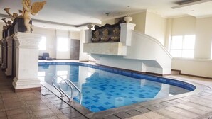Une vaste piscine intérieure dont le carrelage bleu clair forme un motif attrayant, entourée de colonnes blanches et agrémentée d’un escalier décoratif.