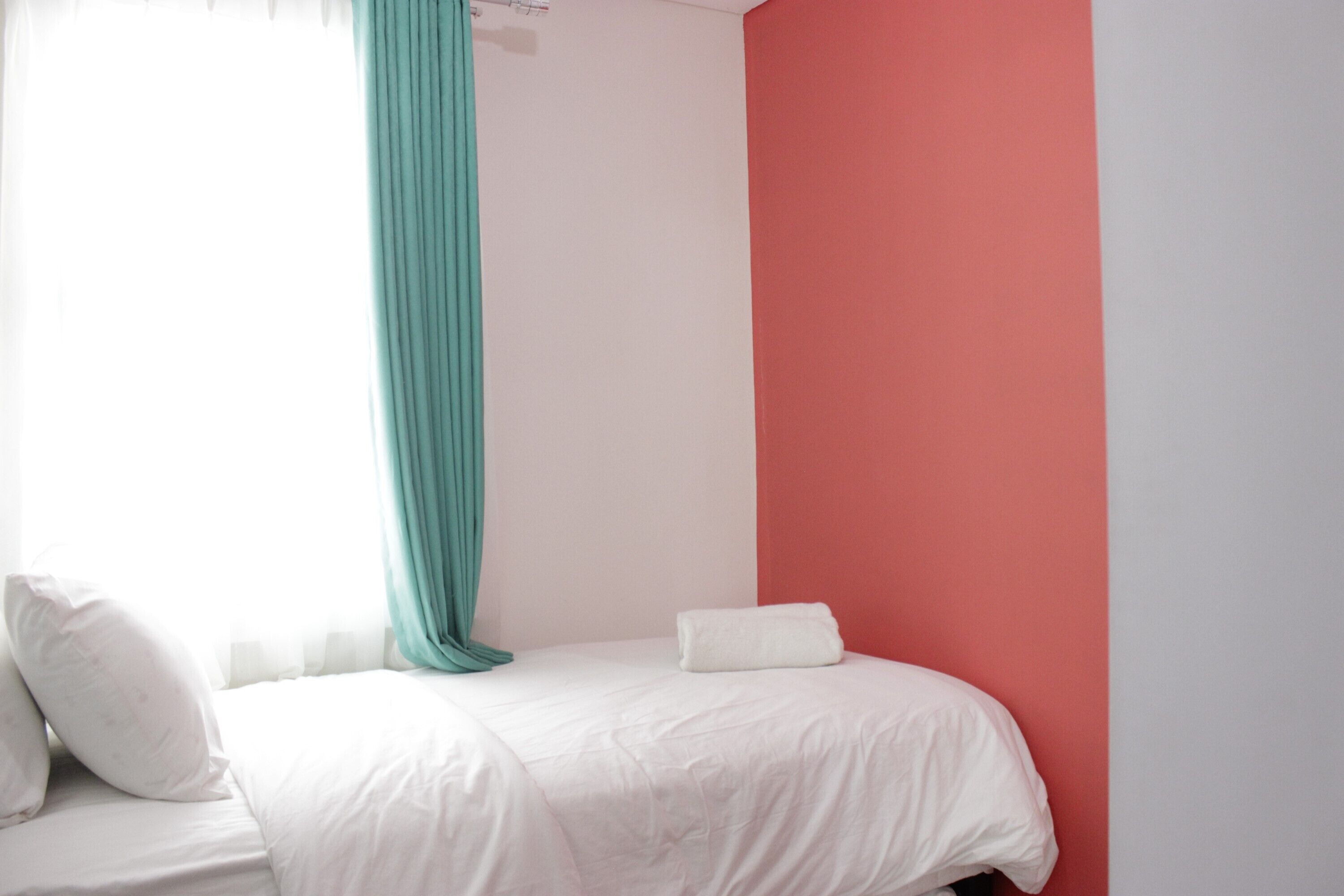 A bedroom with a bed, white bedding, a teal curtain, and a red wall.
