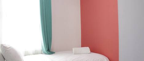 A bedroom with a bed, white bedding, a teal curtain, and a red wall.