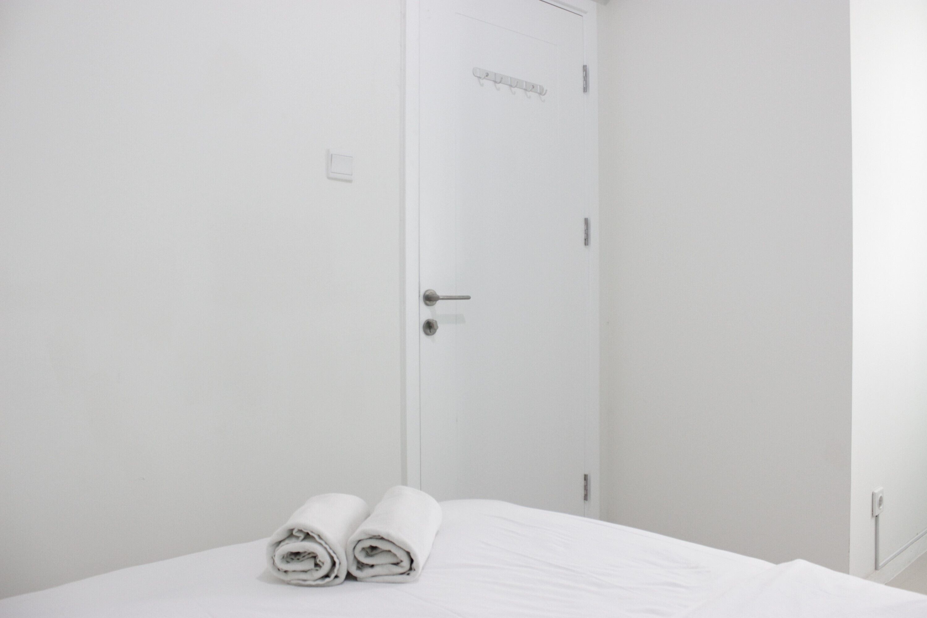 Een witte kamer met een bed, een deur en twee opgerolde handdoeken op het bed.