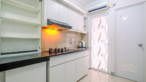 A modern kitchen with white cabinets, a black countertop, a gas stove, a sink, and a built-in oven. - Furnished Green Pramuka 1BR Apartment with Modern Style and City View (Jakarta)
