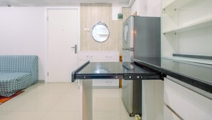 A modern kitchen with a black countertop, stainless steel appliances, and a wooden wall panel. - Furnished Green Pramuka 1BR Apartment with Modern Style and City View (Jakarta)
