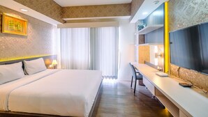Habitación de hotel con una cama grande, un escritorio con silla, un televisor de pantalla plana y una ventana con cortinas.