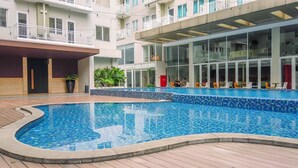Una piscina con solárium empedrado, una zona de estar cubierta y un edificio con balcones y amplias ventanas.