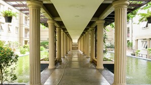 A corridor with columns, a water feature, and hanging plants. - Spacious 3BR Residence at Grand Palace Kemayoran Apartment (Jakarta)