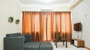 A living room with a sectional sofa, a small table, a TV, and a wooden cabinet. - Spacious 3BR Residence at Grand Palace Kemayoran Apartment (Jakarta)