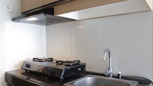 A kitchen with a gas stove, stainless steel sink, and wooden cabinets. - Spacious 2BR Apartment Gateway Pasteur near Exit Toll 23 (Cimahi)