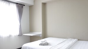 A neatly made bed with white linens and a rolled towel, a window with sheer curtains, and a white shelf against the wall. - Spacious 2BR Apartment Gateway Pasteur near Exit Toll 23 (Cimahi)