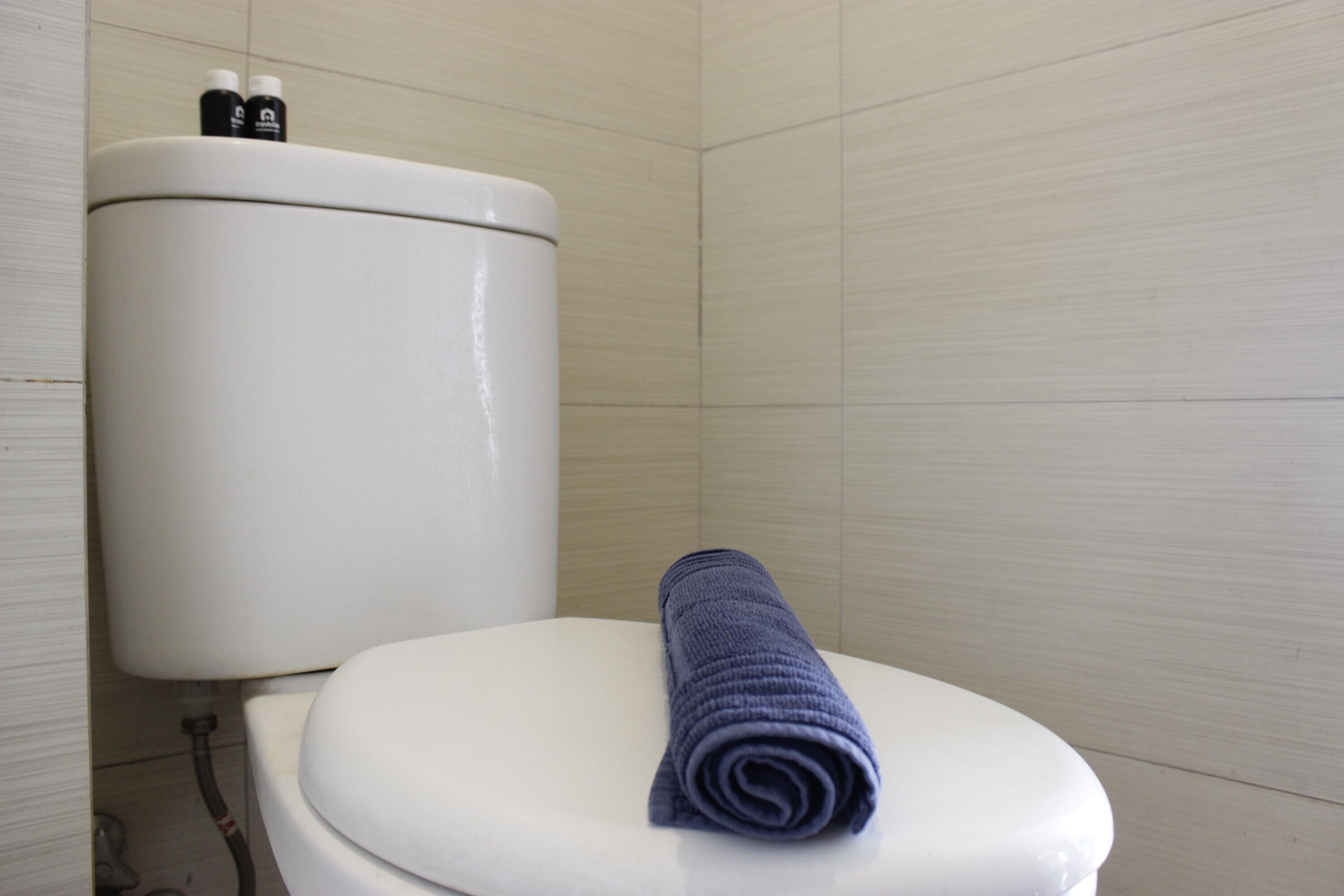 A toilet with a rolled towel on the seat and two bottles on the tank.