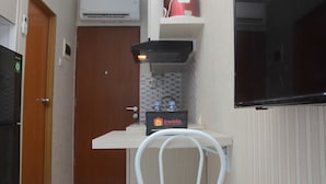 A compact kitchenette with a refrigerator, a microwave, a small sink, and a cabinet with a red container.