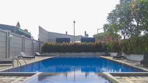 A swimming pool with lounge chairs, a modern building with satellite dishes, and a tree with pink flowers.