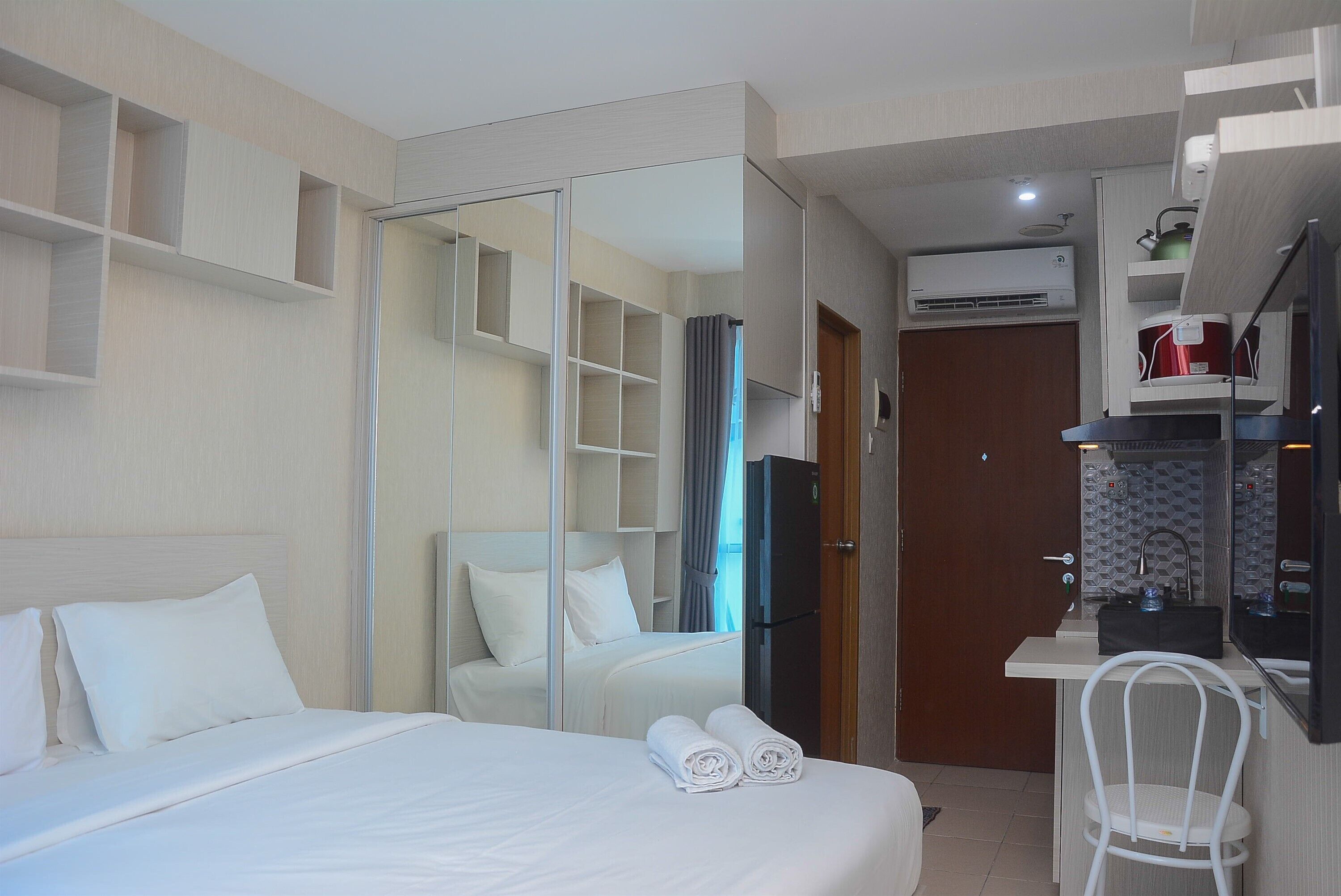 A hotel room with a bed, a desk, a chair, a wardrobe, and an air conditioning unit.