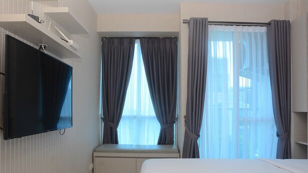 A hotel room with a bed, a TV mounted on the wall, a window with curtains, and a view of the outside.