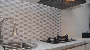 A kitchen with a modern design, featuring a geometric patterned backsplash, a stainless steel sink, and a gas stove.