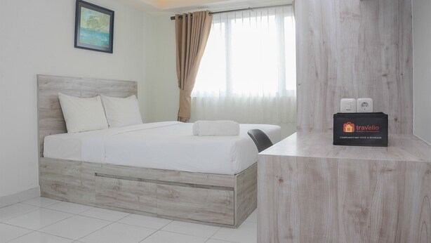 Une chambre d’hôtel avec un lit en bois, une petite table sur laquelle se trouve un sac de voyage, et une fenêtre avec des rideaux.