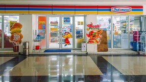 Un supermarché avec une devanture colorée, un personnage de dessin animé et une enseigne indiquant « Buah Potong ».