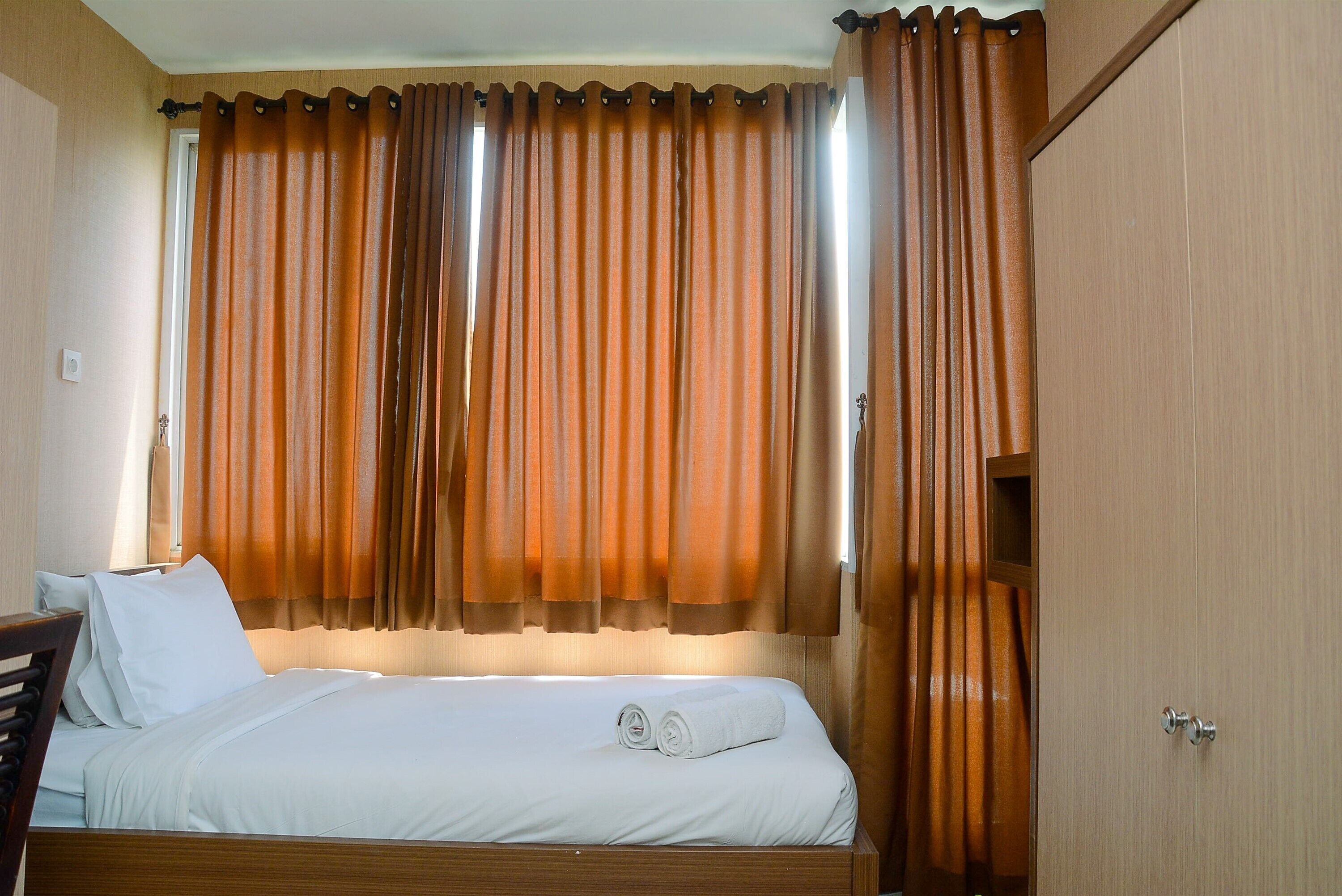 Una camera d'albergo con un letto rifatto, una testiera in legno e un'ampia finestra con tende.