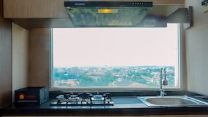 A kitchen with a gas stove, a sink, and a window overlooking a cityscape. - Cozy and Minimalist Studio Apartment at Saladdin Mansion (Depok)