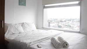 Ein Hotelzimmer mit großem Fenster, einem Bett mit weißer Bettwäsche, einer Fernbedienung und einem Handtuch auf dem Bett.